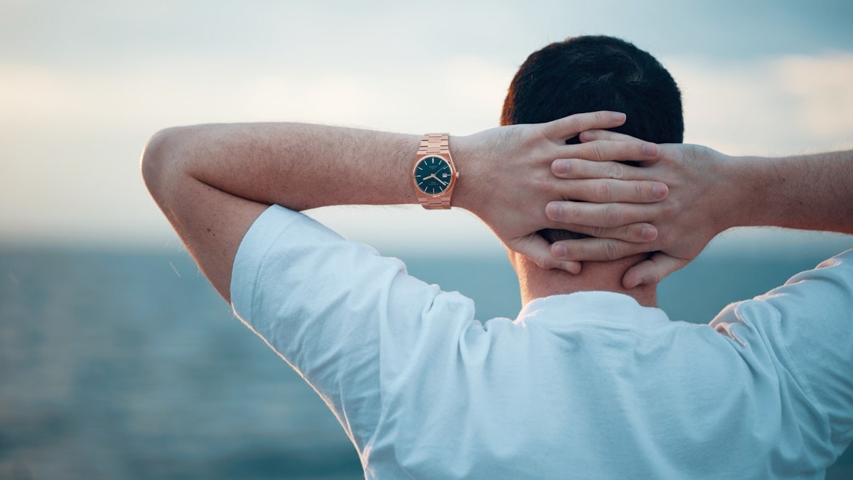 Man relaxing with hands behind head, watching the sea.